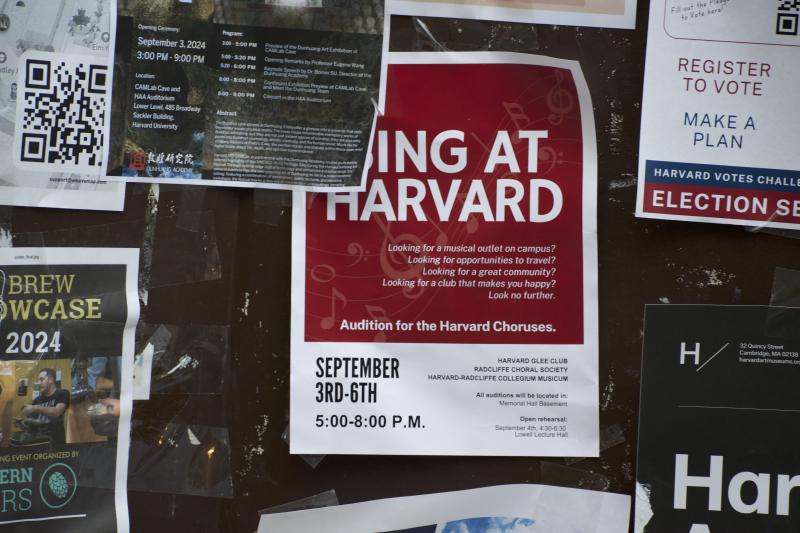 Picture of a red poster with the words "SING AT HARVARD" on it taped on a billboard among other posters.