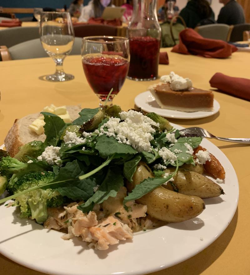 Picture of a plate of Thanksgiving-style food. There's a glass container with red juice and pumpkin pie on the table.