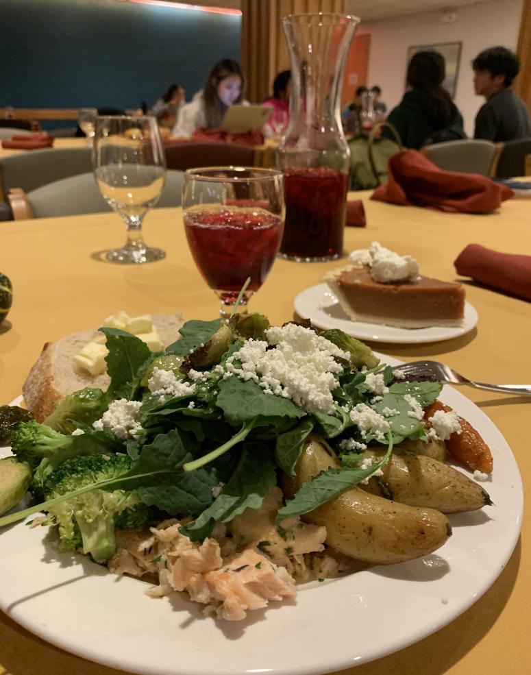 Picture of a plate of food with salmon, roast potatoes, and salad with a glass of cranberry juice in the background.