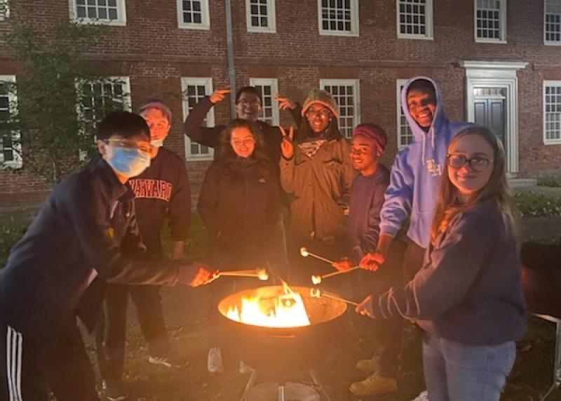 Group picture of Massachusetts Hall residents roasting marshmallows beside a fire pit.