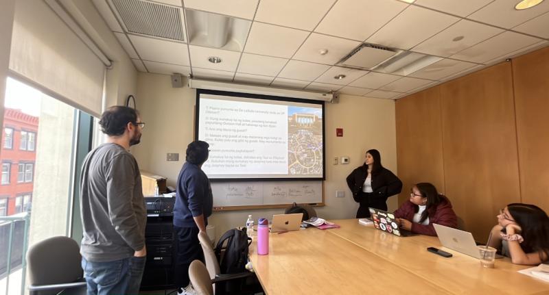 Students sitting and standing around a table looking at a presentation