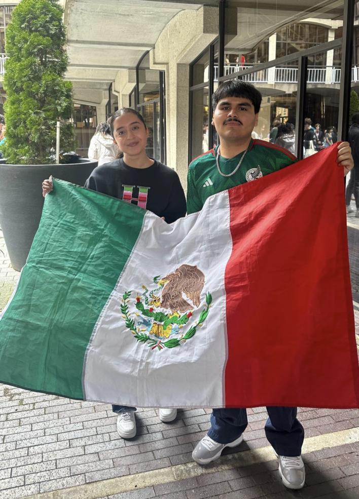 Picture of RAZA's social chairs holding the Mexican flag outside of the student activities fair during Visitas.