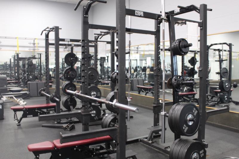 Weightlifting area with racks, barbells, and benches in a gym.