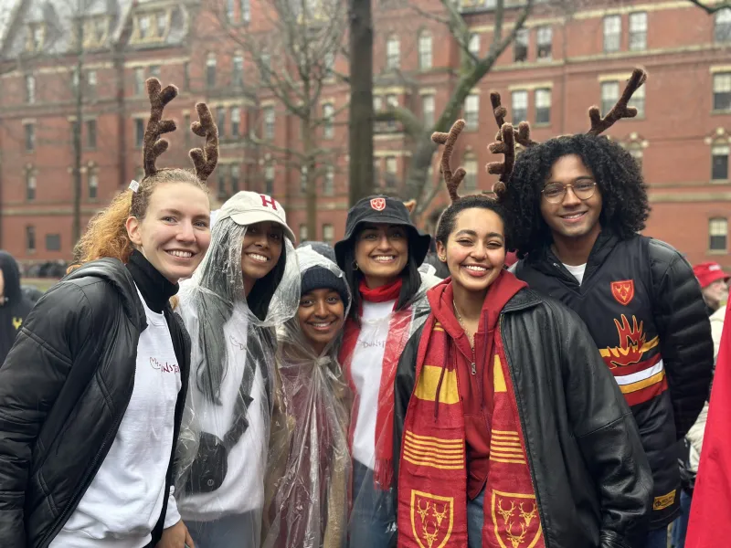 A group of people smiling outdoors, wearing reindeer antlers and themed attire, with a brick building in the background.