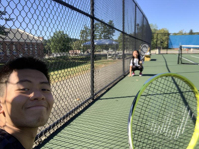 Selfie picture of Raymond and his sister on a tennis court holding up their tennis rackets.