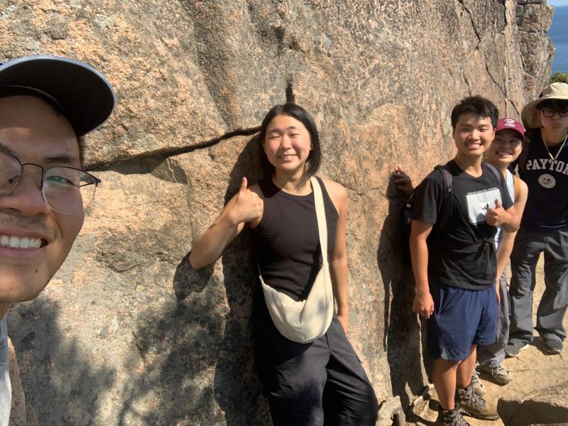 Selfie picture of Raymond and his friends clinging onto a stone wall while hiking the Beehive Trail at Acadia National Park.