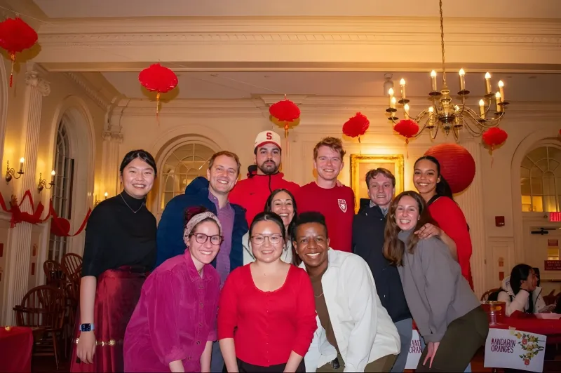 A group of individuals, including faculty deans, tutors, and students, smiling together in a decorated room with red lanterns.