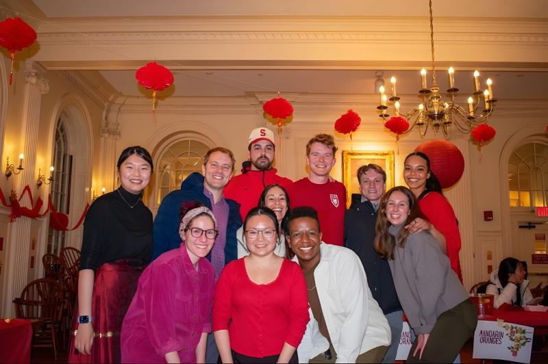 A group of individuals, including faculty deans, tutors, and students, smiling together in a decorated room with red lanterns.