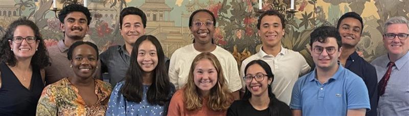 A group of people smiling and posing together indoors, in front of a decorative mural.