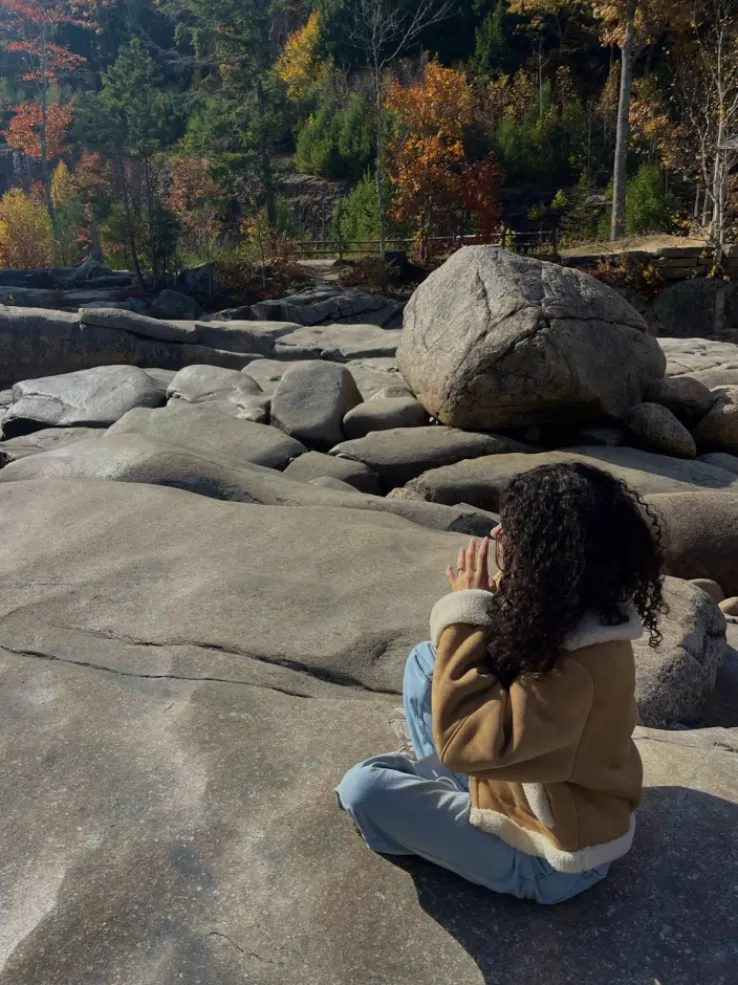 Student sitting on a rock on a scenic trail during the fall.