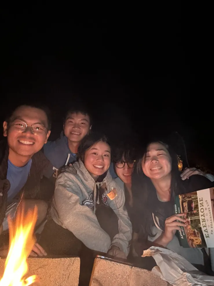 A picture of Raymond and his friends surrounding the campfire, smiling at the camera.