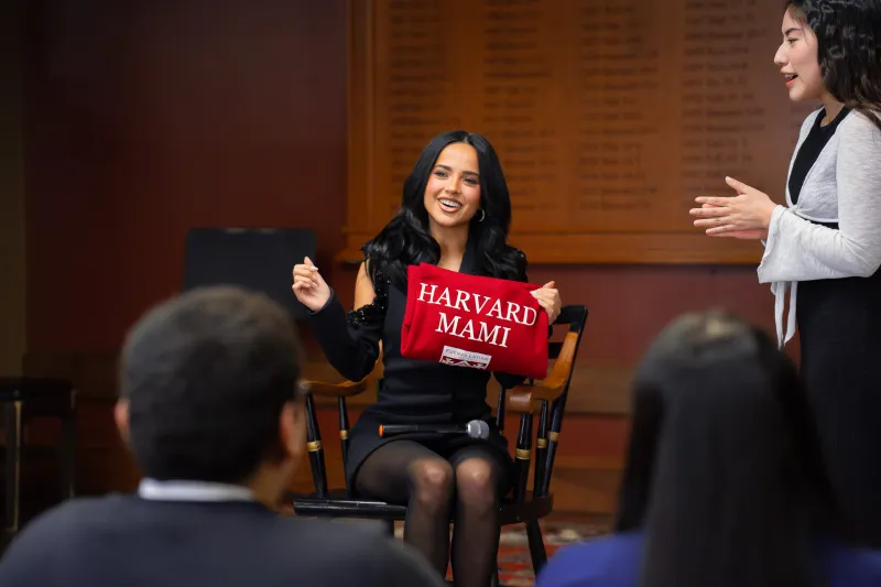 This is a picture of Becky G holding a red sweater that has "Harvard Mami" written on it