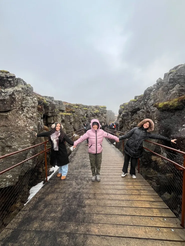 Three people holding hands and standing on a bridge. The two people at the edges are touching tectonic plates.