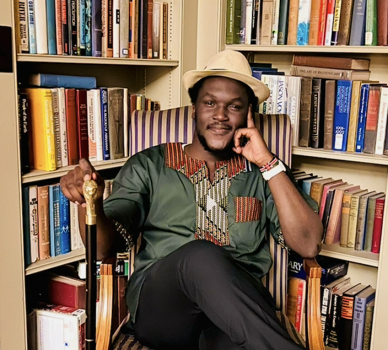Photo of David sitting amongst some bookcases filled with books