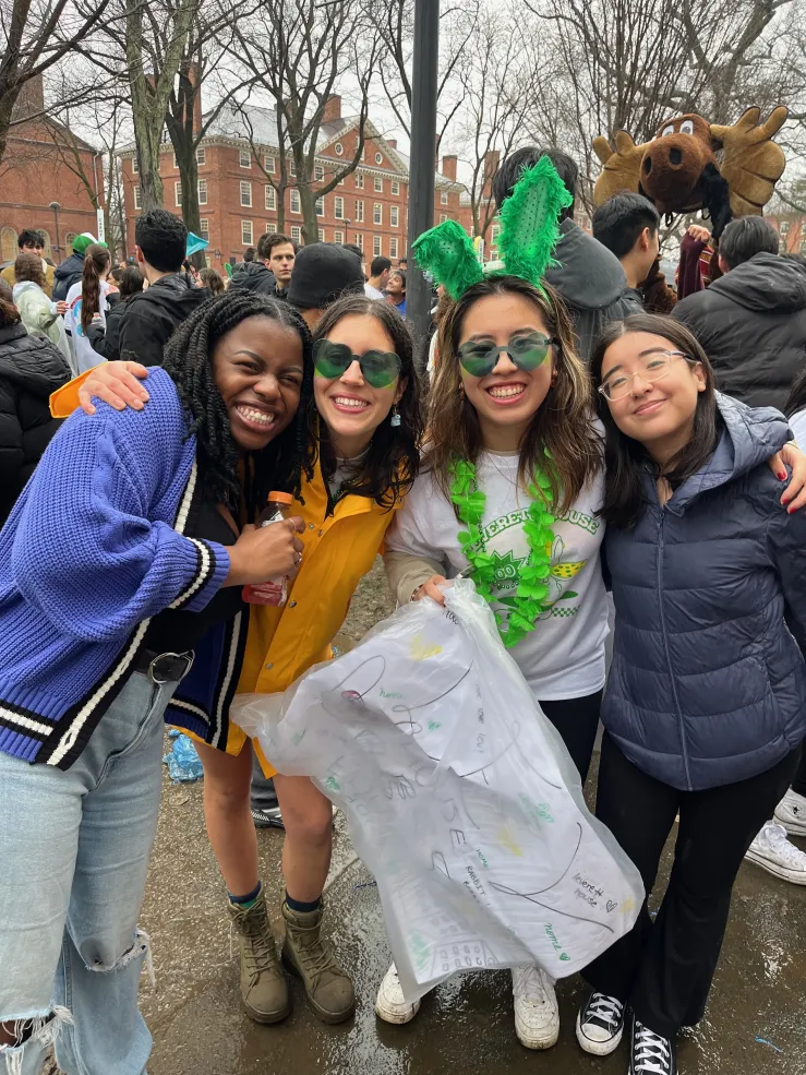 A group of four girls smiling and wearing Leverett House merchandise in Harvard Yard on Housing Day 2024.