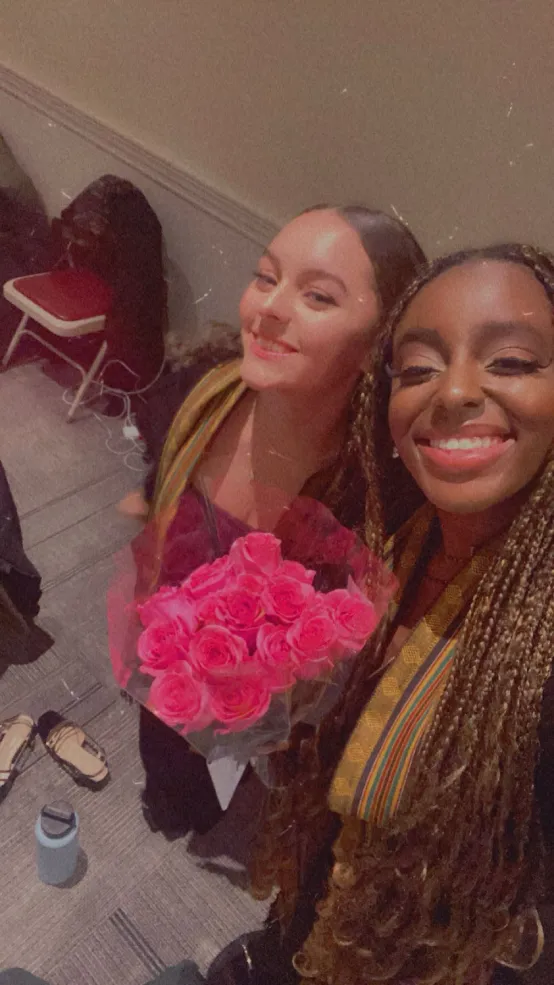 Two young women holding a bouquet of pink roses and smiling