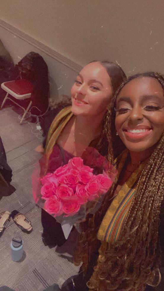Two young women holding a bouquet of pink roses and smiling
