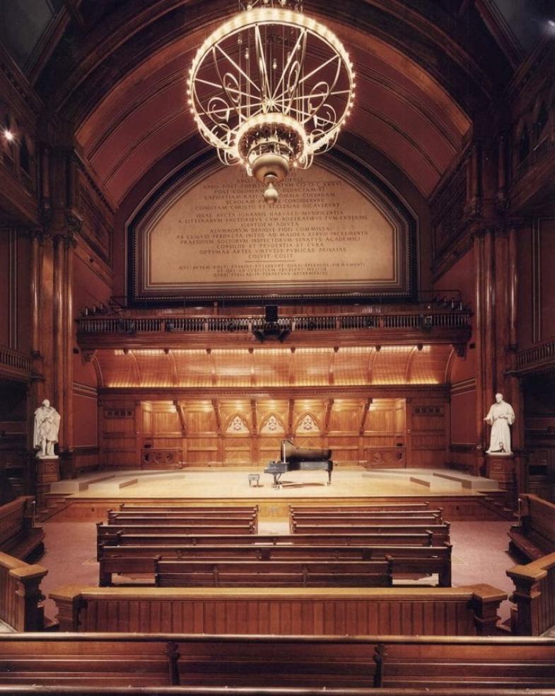 Empty Sanders Theatre with warm lighting, wooden interior, and intricate architectural details, highlighting the elegance of the historic performance space.