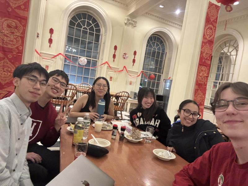 Meena with her Bach Society Orchestra friends during a casual gathering outside of rehearsal sitting around a table, smiling and enjoying time together.