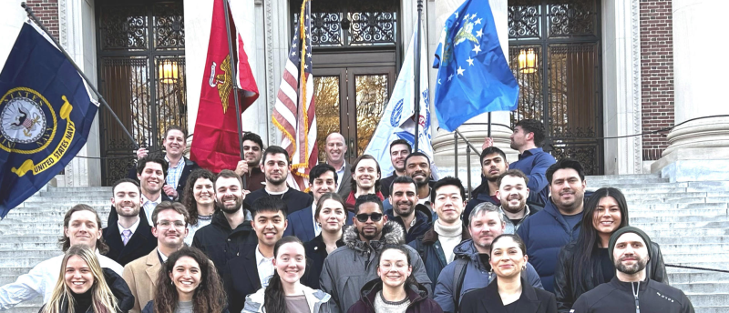 A group of people stand together on steps outside a building, holding several flags.
