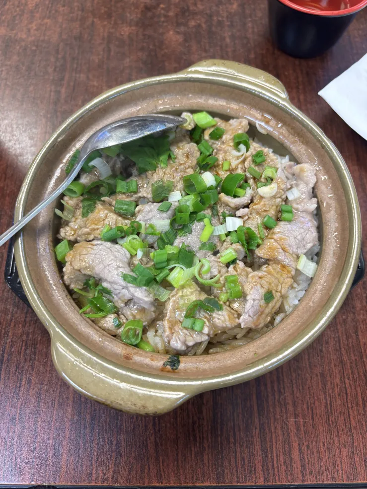 A small clay pot that filled with rice and cooked beef chunks, topped with scallions.