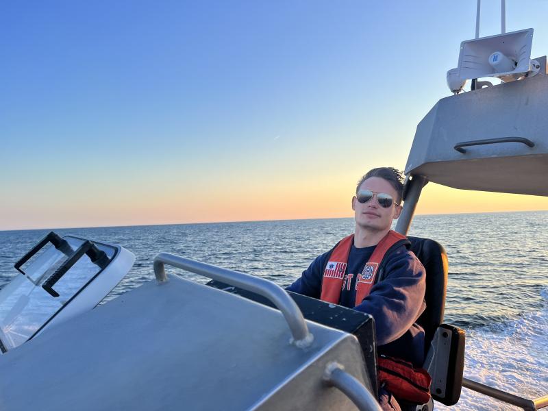 Dmitry driving a boat for the crew and mission, with sunglasses on against the sunset behind him.