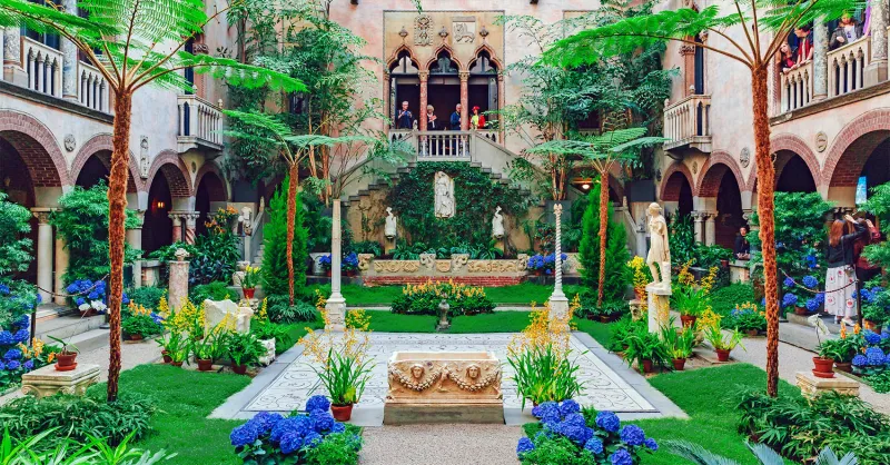 Pictured is the Isabella Steward Gardner Museum Courtyard! There are various small trees, grassy areas, and flowers.