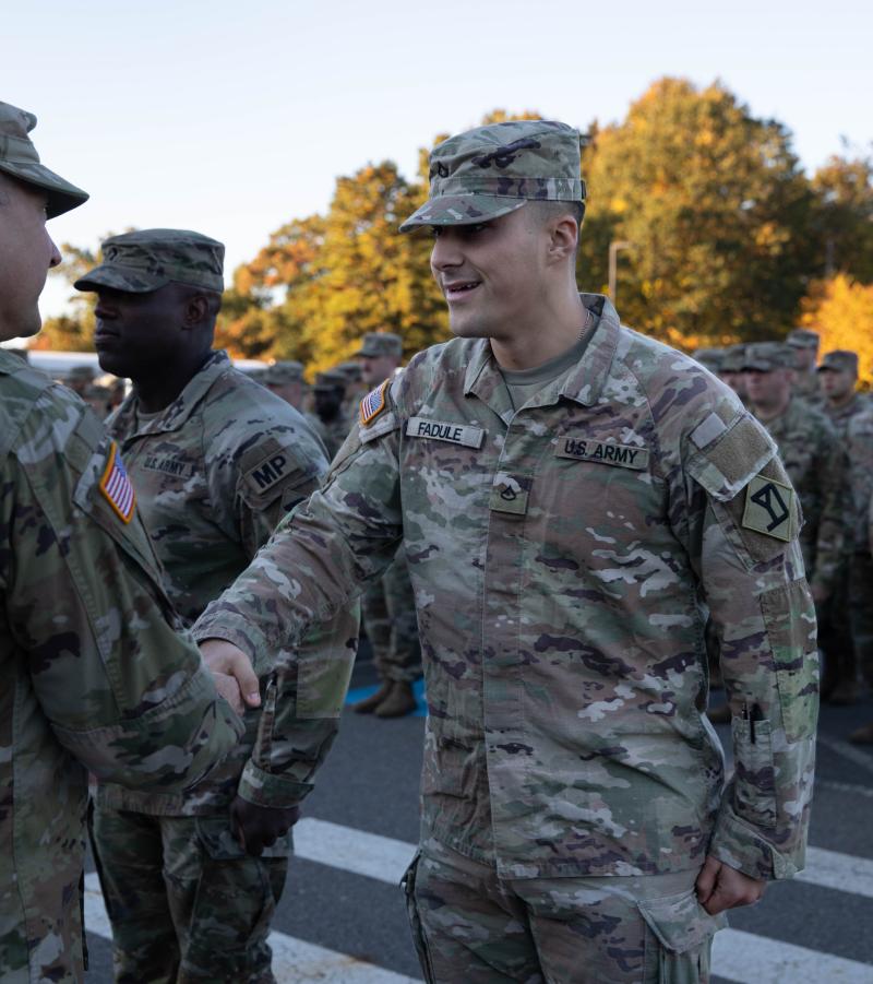 Dressed in his camoflauge uniform, Fadule smiles and shakes the hand of a fellow serviceman as he receives an award. 