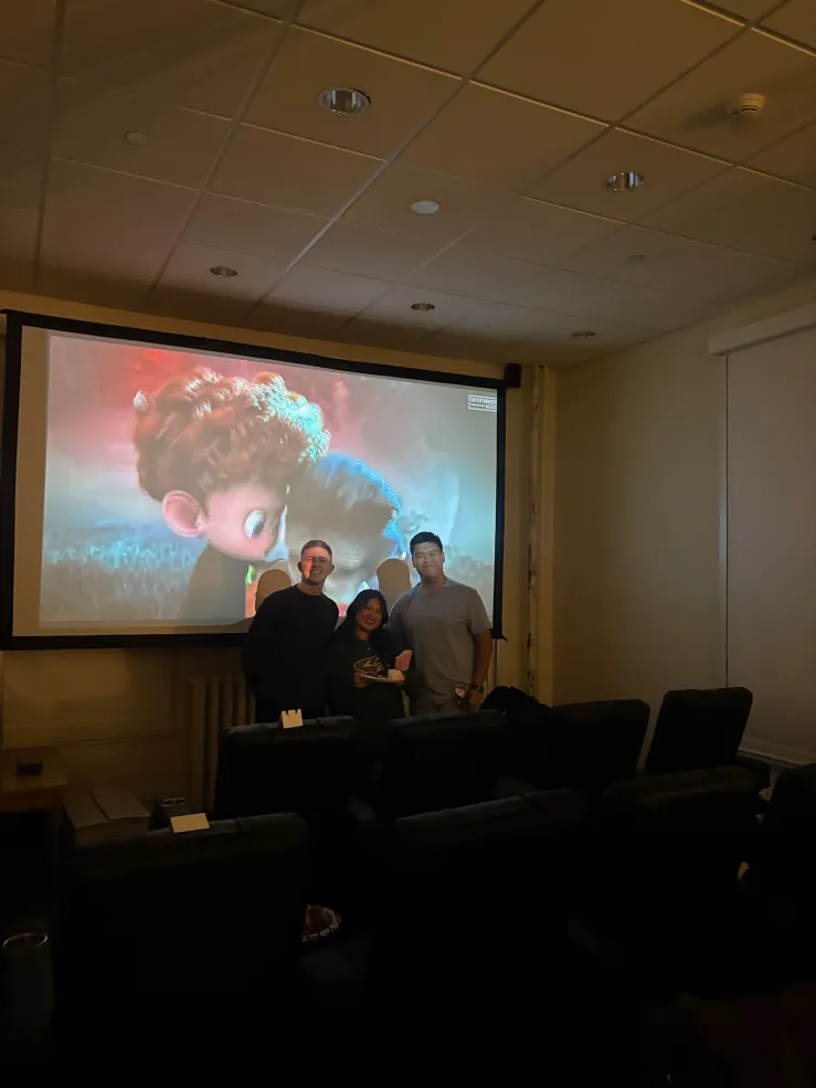 3 people standing in between movie theater chairs and a projector screen.