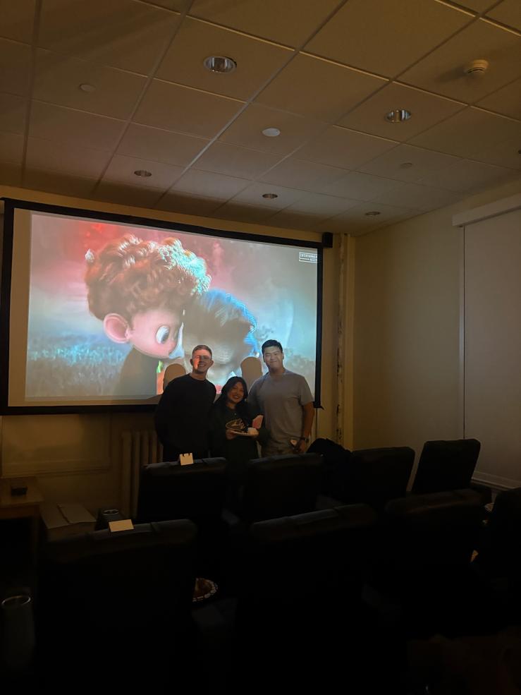 3 people standing in between movie theater chairs and a projector screen.