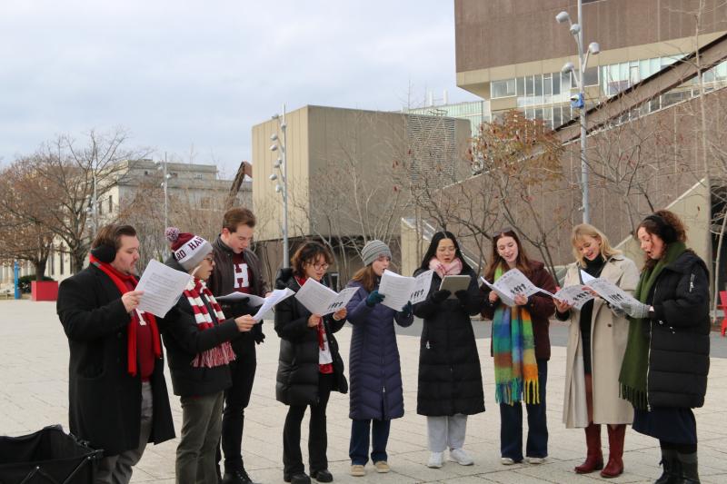 A group of student singers read sheet music while caroling outside on Harvard's campus.