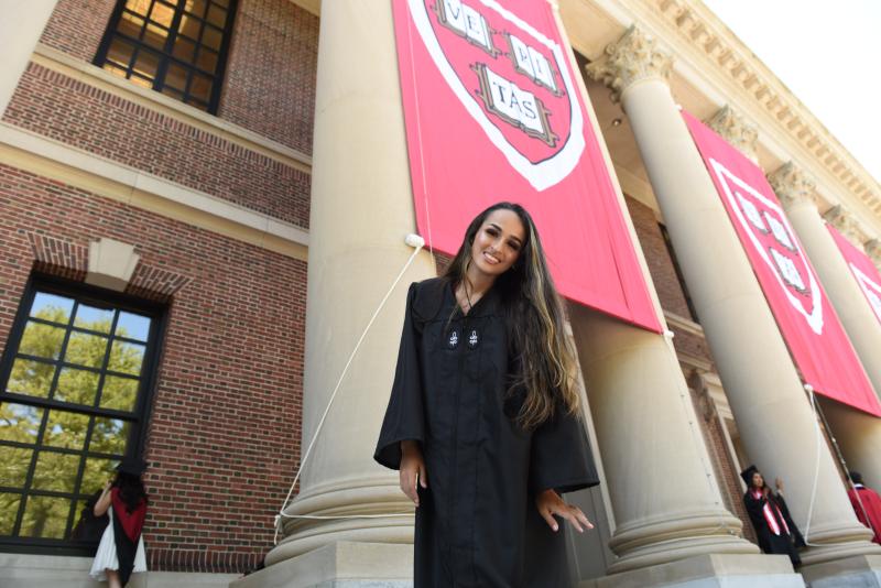 Jazz Jennings standing on the steps of Widener Library in her graduation regalia.