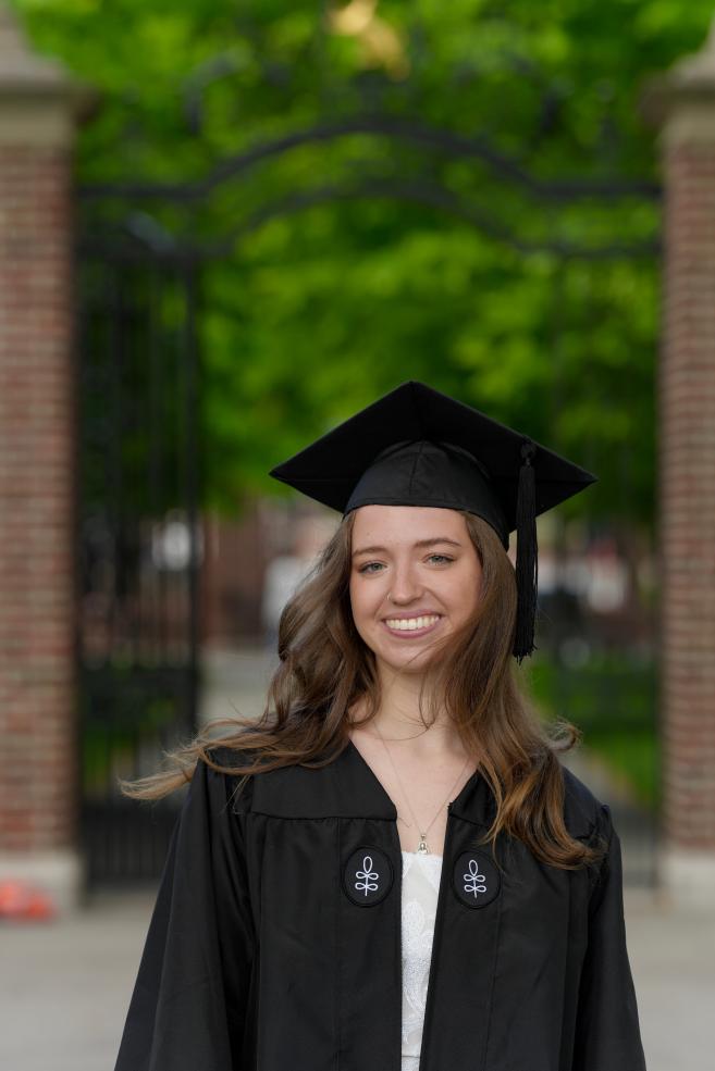 Naomi Corlette in her graduation regalia next to the Harvard gates.