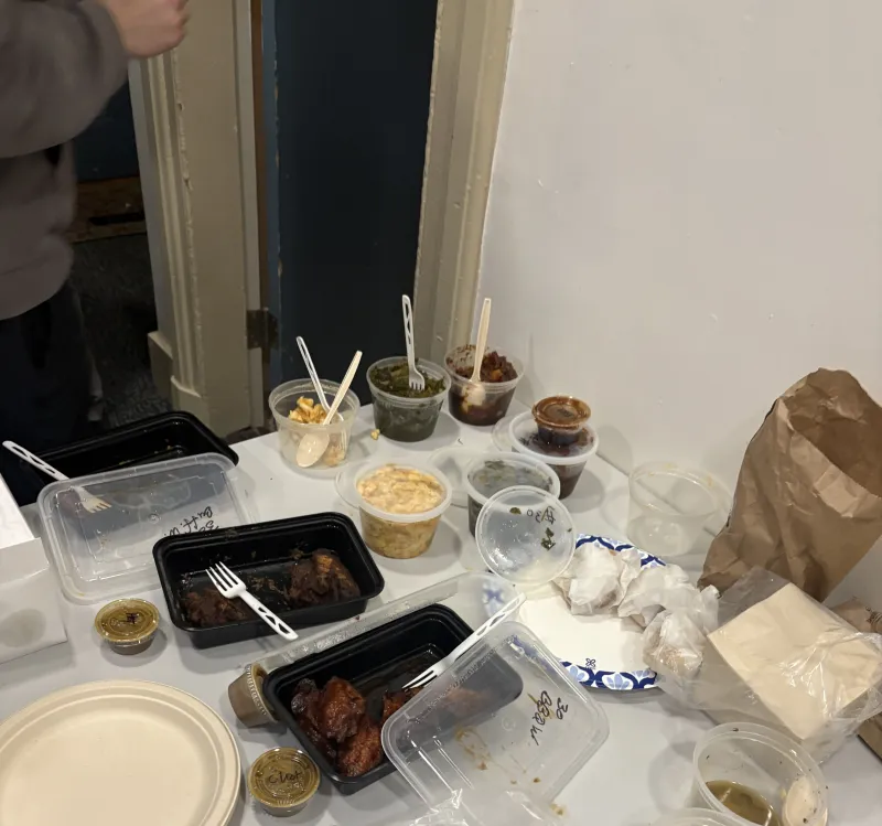 Open containers of Southern food staples (mac and cheese, chicken, greens) on a table.