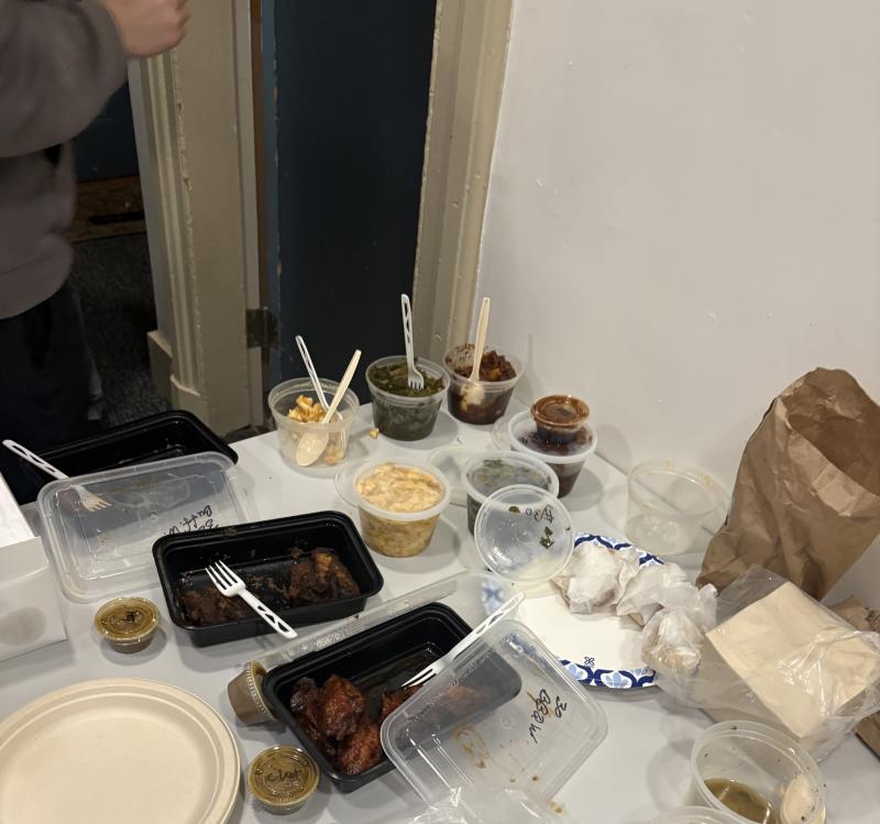 Open containers of Southern food staples (mac and cheese, chicken, greens) on a table.