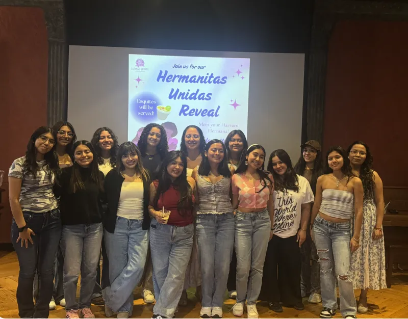A group of female students in front of drop-down board that reads "Hermanitas Unidas Reveal."