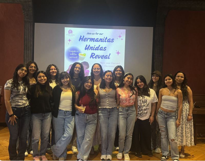 A group of female students in front of drop-down board that reads "Hermanitas Unidas Reveal."