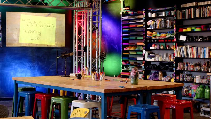 A view inside the colorful Bok Center, featuring a large wooden table, a wall of colorful materials, and monitor screen that says the Bok Center.