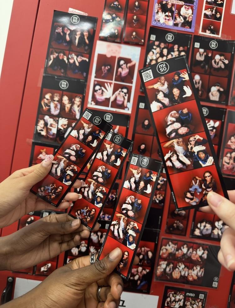 Four hands holding prints from a photobooth with a red background