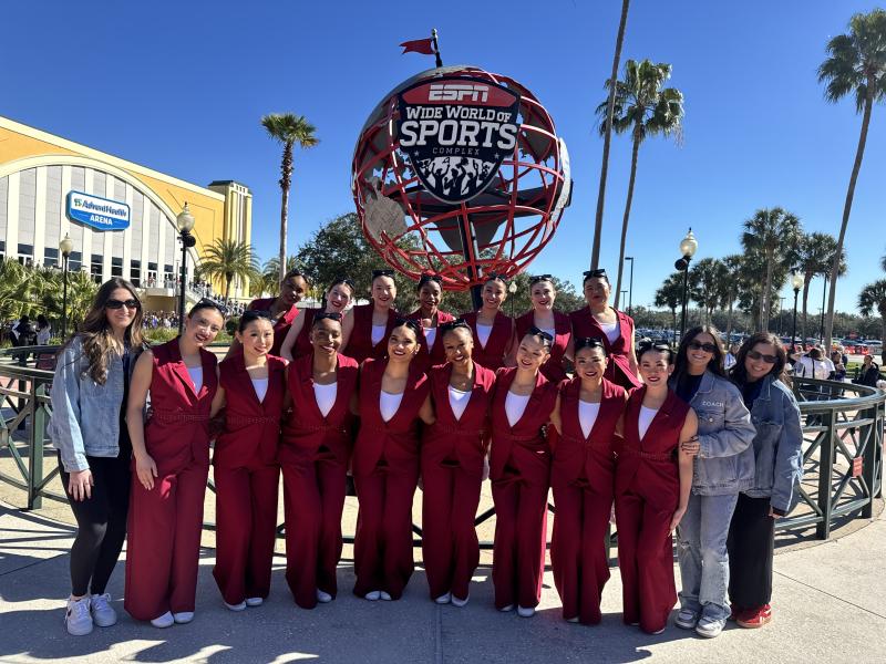 The Harvard Dance Team dressed in matching red jumpsuits standing in front of the ESPN Wide World of Sports Complex sign in Orlando, Florida.
