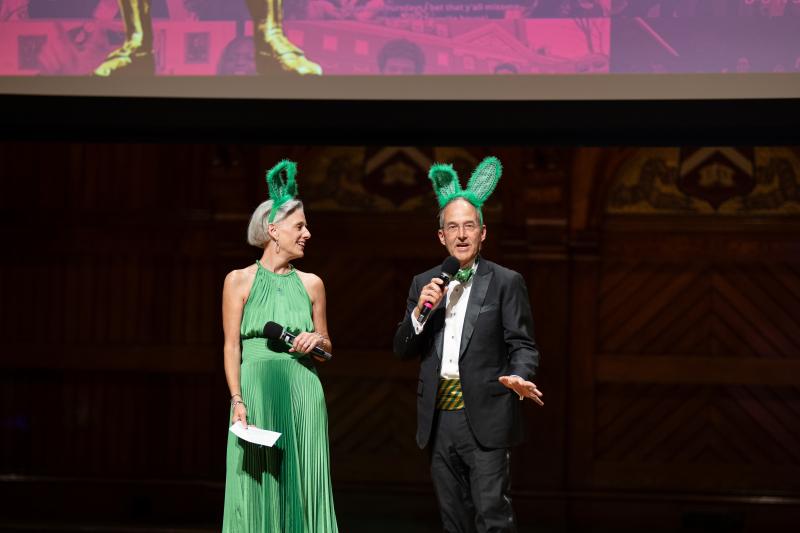 Leverett House Faculty Deans Eileen Reynolds & Dan Deschler onstage wearing green rabbit ears for Leverett.