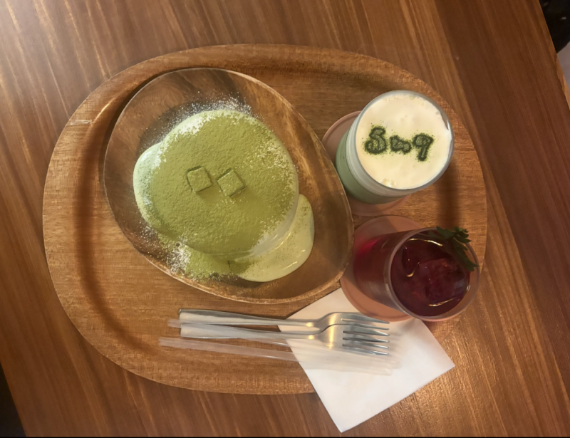 Spread of green souffle pancake with two drinks and two forks on a wooden tray, set on a brown wooded table. 