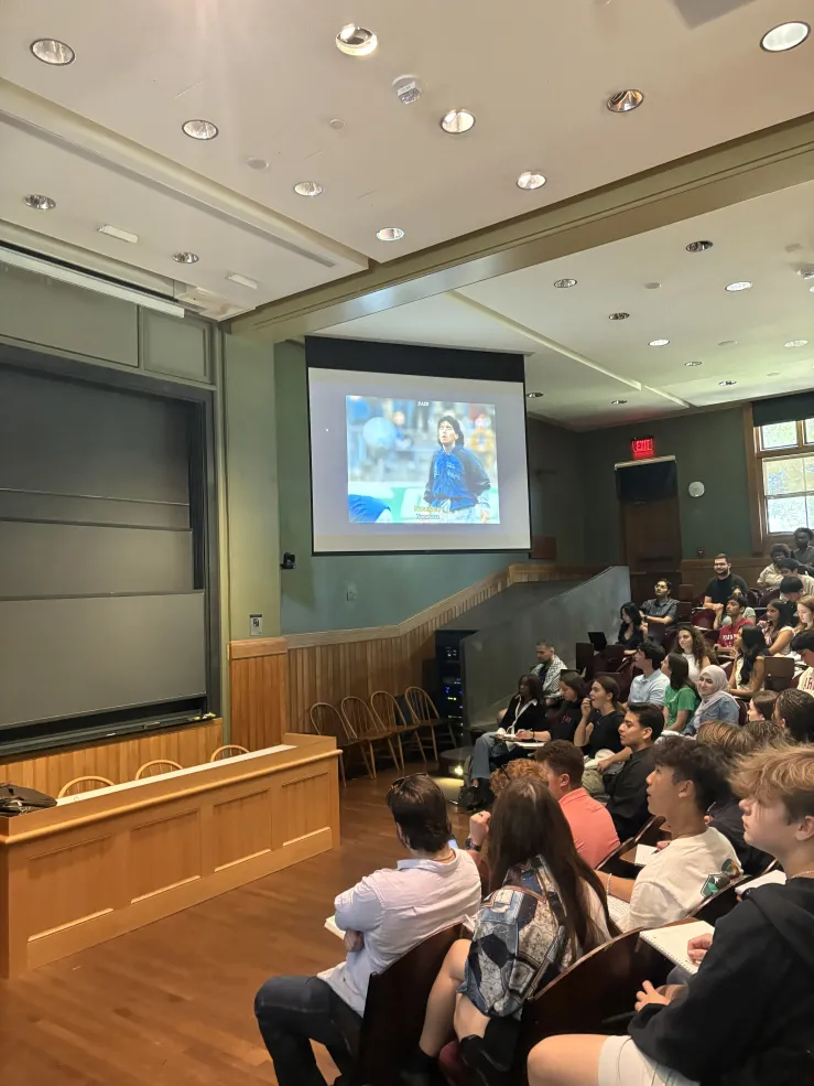 Group of students in lecture hall, sitting in front of projector.