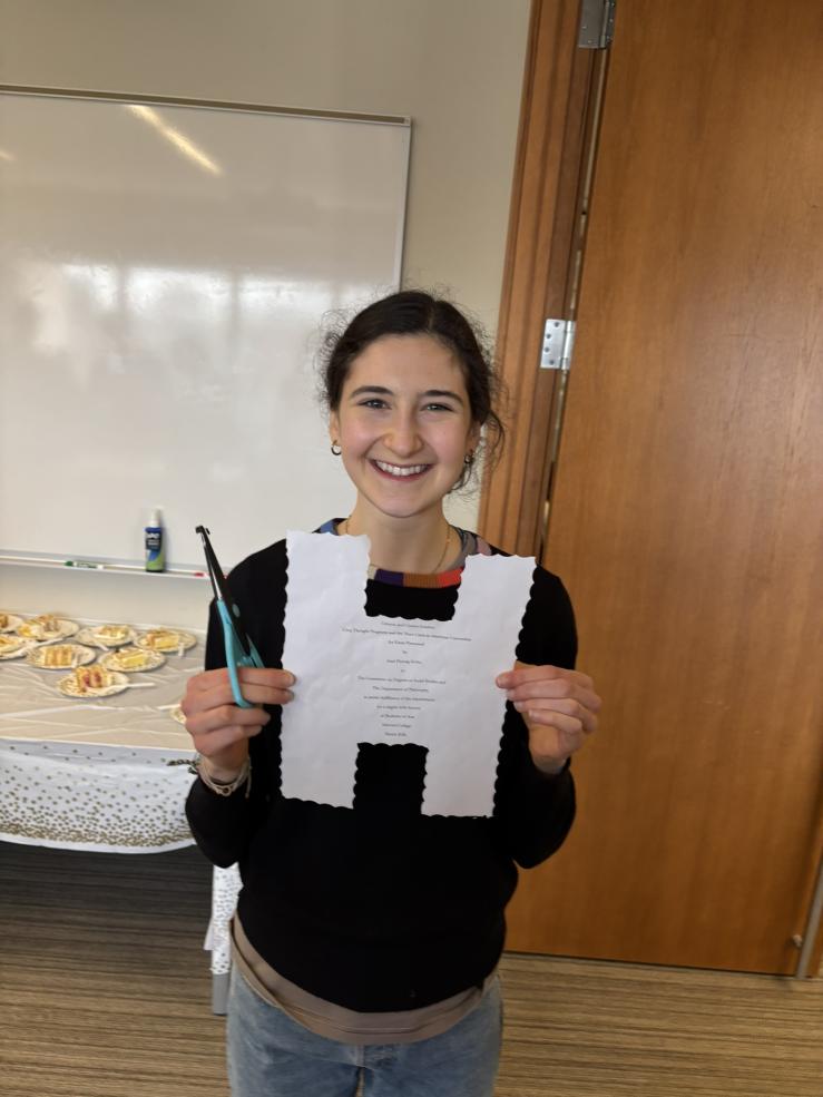 Ari holding up a letter H that she cut out of her thesis title page.