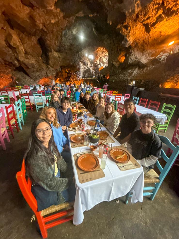 Students inside a cave at a large table, having a meal together.