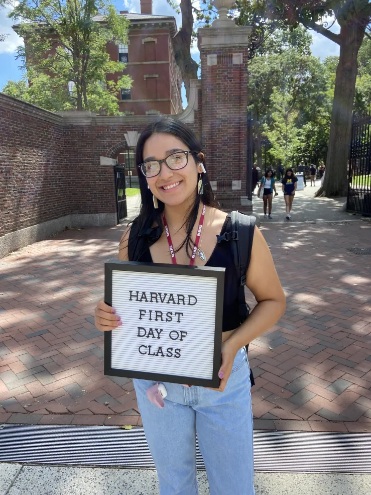 Lizbeth as a first year on her first day of class. She is holding a sign that says "Harvard First Day of Class."