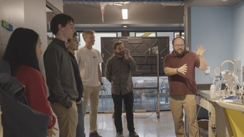 Students learning from a professor who is explaining a project to them.