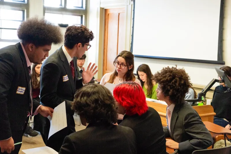 Students standing speaking to seated students engaging in discussion.