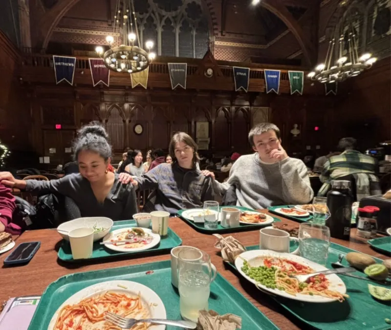 Group of students in the dining hall, holding one another's shoulders, with trays in front of them 