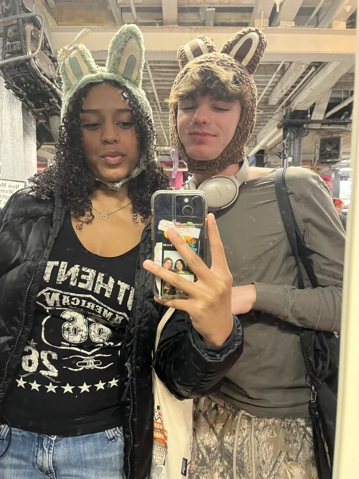 Two people photographed in a mirror wearing fuzzy ear pieces. The girl on the left is holding the phone. Both are posed facing the phone camera.